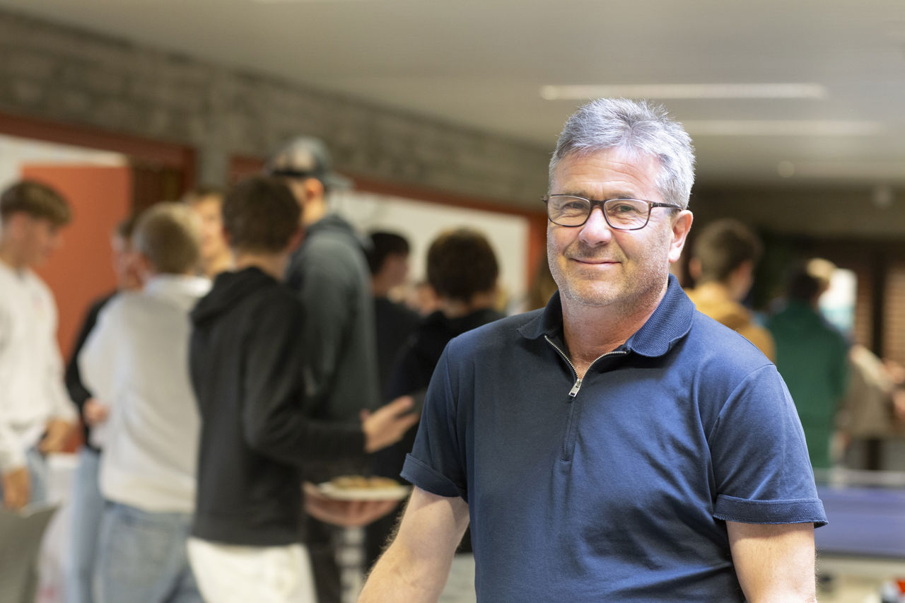 Miljøkoordinator Helge Øren smiler medan han rører i ei stor panne med kakao. han er på personalkjøkjkenet og lagar kakao til alle på huset, både lærar ar og elevar.