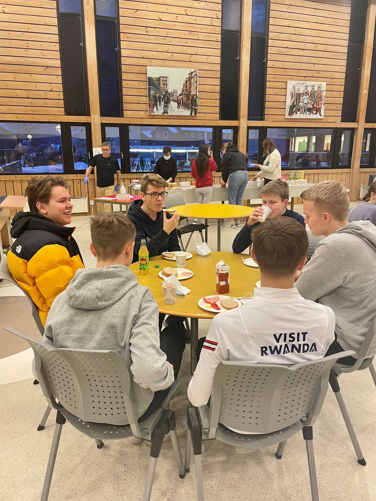 Seks elevar sit samla rundt eit bord i kantina og et skulefrokost. I bakgrunn kan ein sjå fleire elevar som forsyn seg med skjebver og pålegg.