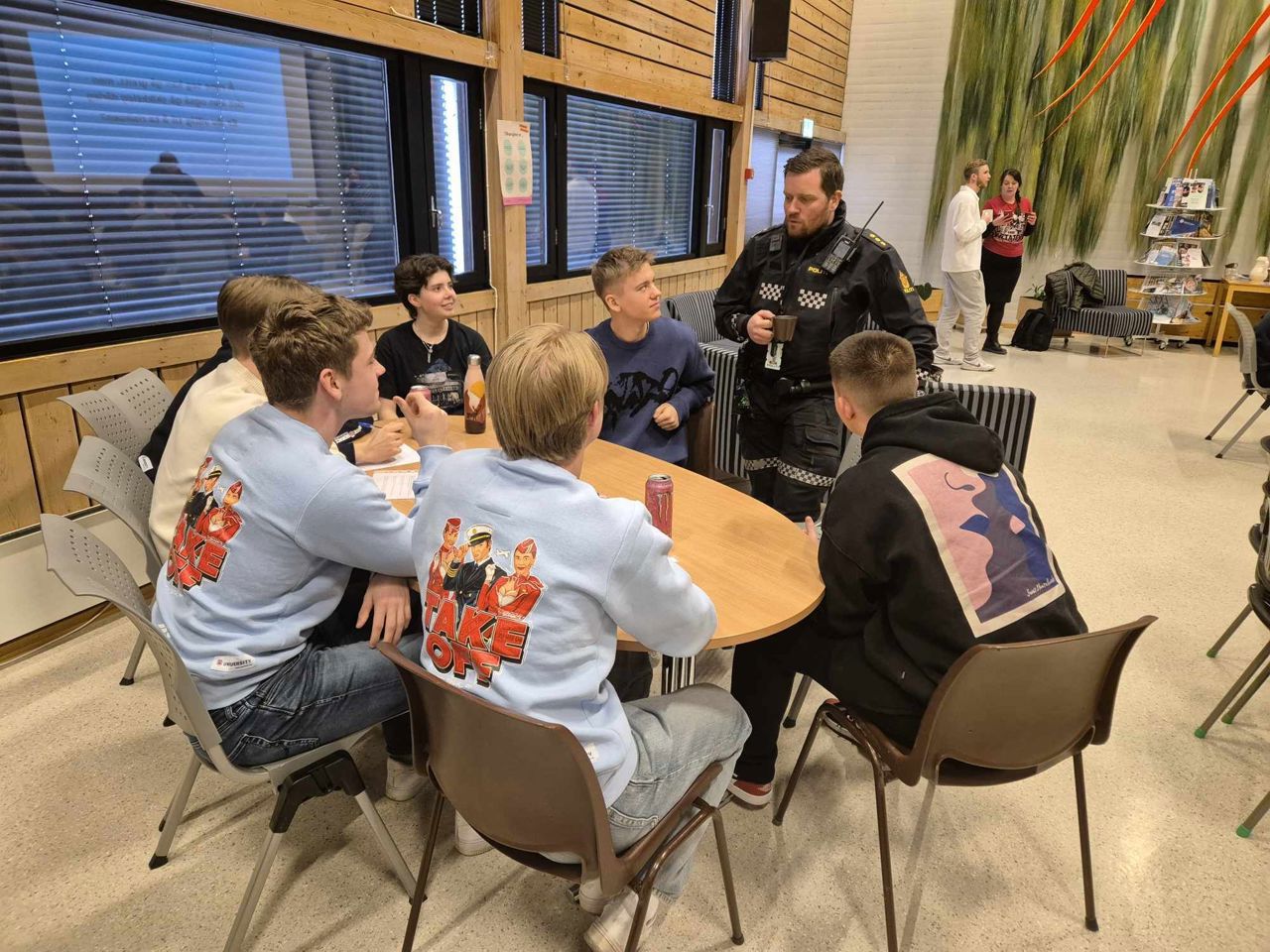 Gruppearbeid der elevane sit rundt eit bord og er i dialog med ein politimann.
