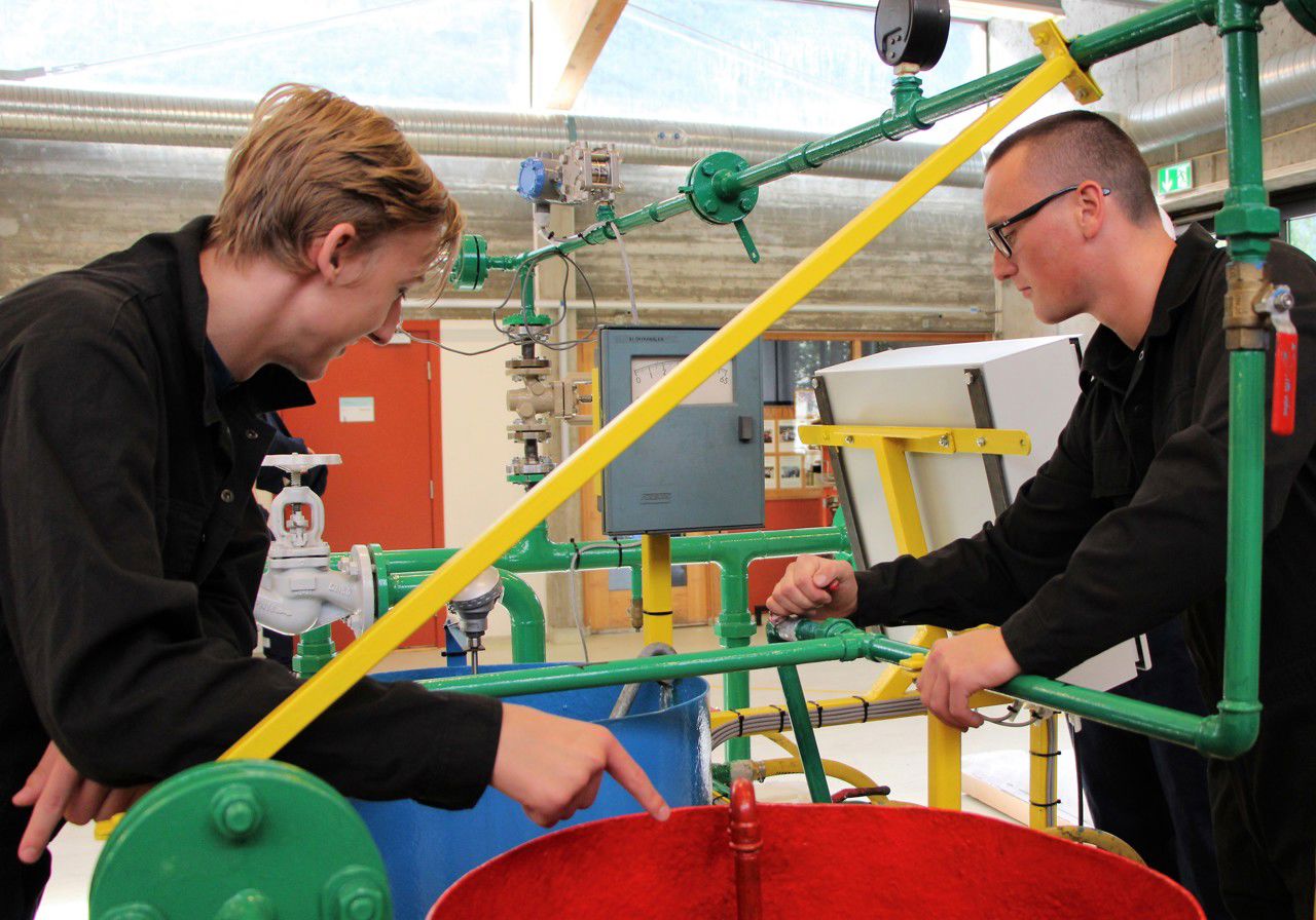 Elevar frå kjemiprosess- og laboratoriefag jobbar med røyrriggen på verkstaden. Det er fire elevar som står rundt riggen. Ein av elevane trykkjer på kontrollpanelet, medan tre andre følger med.