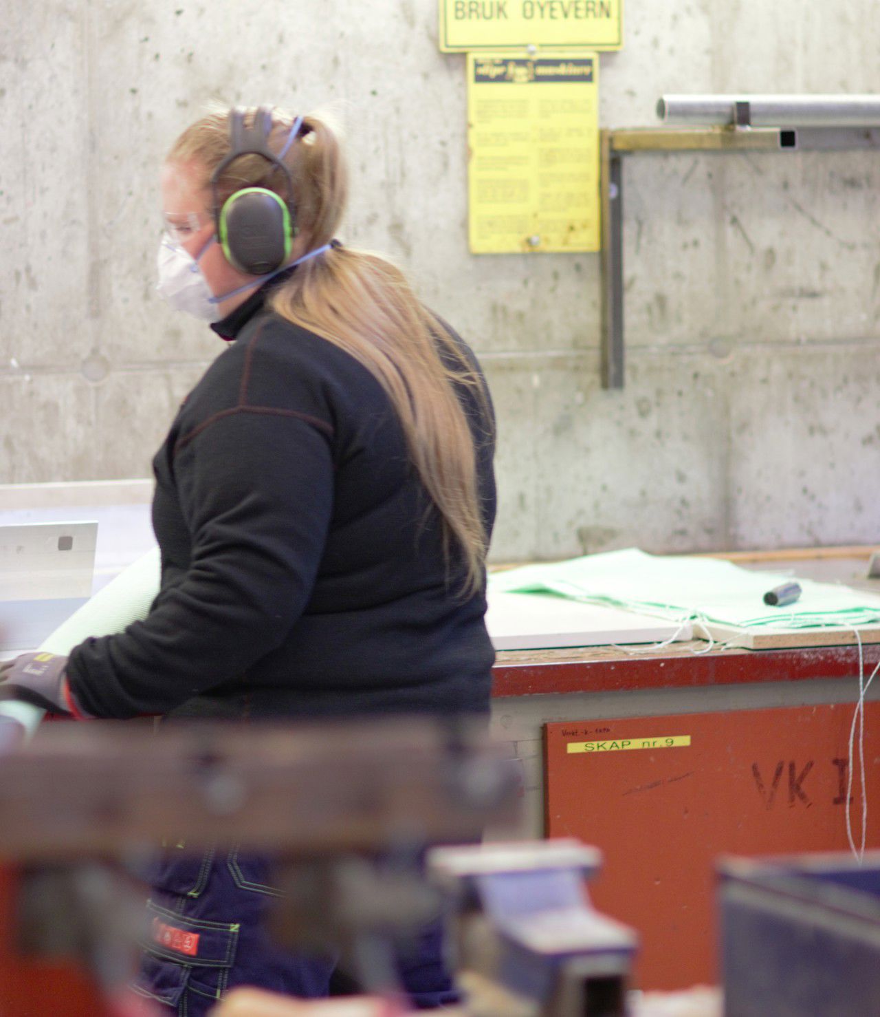 Elev frå  kjemiprosess- og laboratoriefag produserer deksel til aluminiumsomnar for Hydro som er bestilt via elevbedrifta deira. Eleven har langt, lyst hår og og høyrselsvern, og står med ryggen mot kamera.