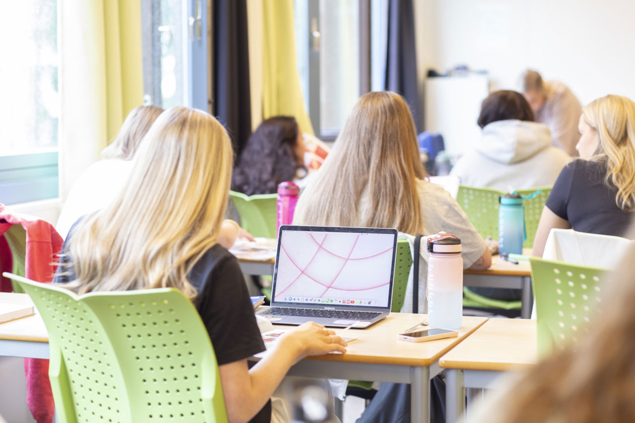 Bilete teke bakfrå i klasserommet. Elevar som sit og jobbar på PC.